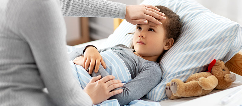 Parent checking forehead of sick child for a fever, a symptom of Measles