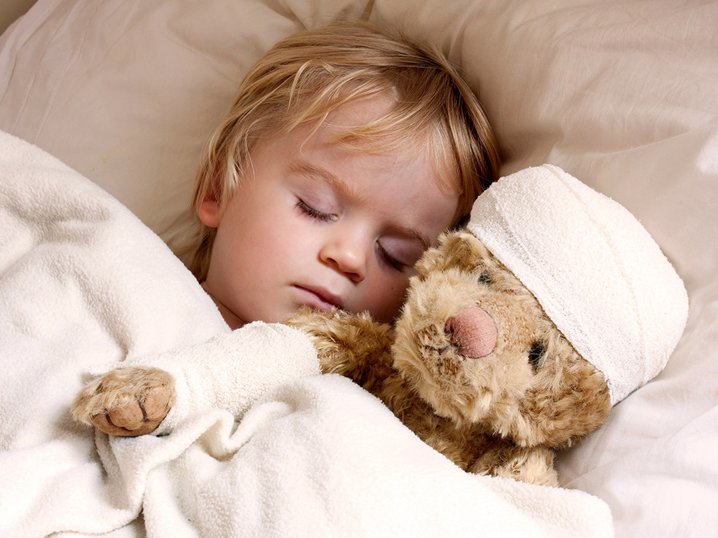 Young child sleeping with teddy bear that has bandages around its head and paw