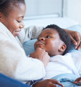 Smiling mother comforting child resting in hospital bed